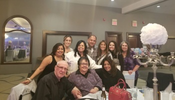 A large smiling family posing together around a table at an indoor celebration.