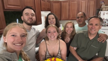 Seven smiling family members pose together in a kitchen around a 21st birthday cake.
