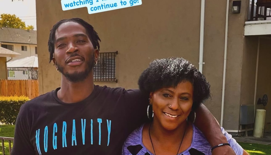 A young Black man in a black t-shirt with his arm around a smiling Black woman in a purple top.