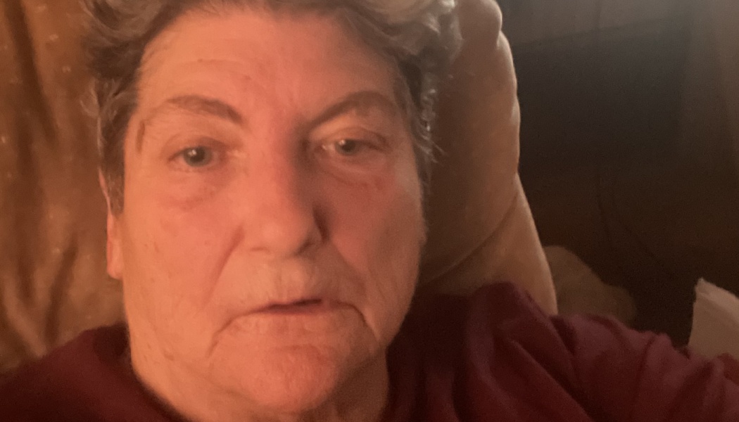 Close-up portrait of an older woman with short grey hair looking directly at the camera.