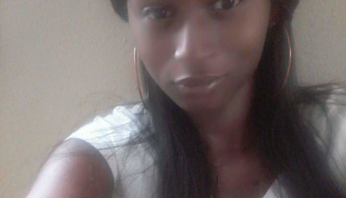 Close-up portrait of a young Black woman with long dark hair and hoop earrings wearing a white top.
