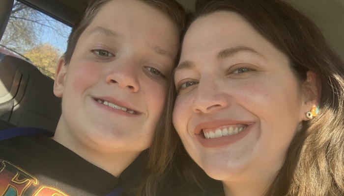 A smiling woman and a young boy posing close together for a selfie in a car.