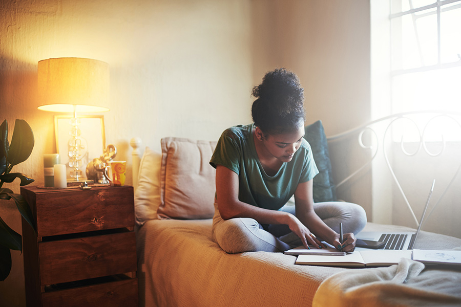 Resident studying on her bed at 4000 Hulen Urban Apartment Homes in Fort Worth