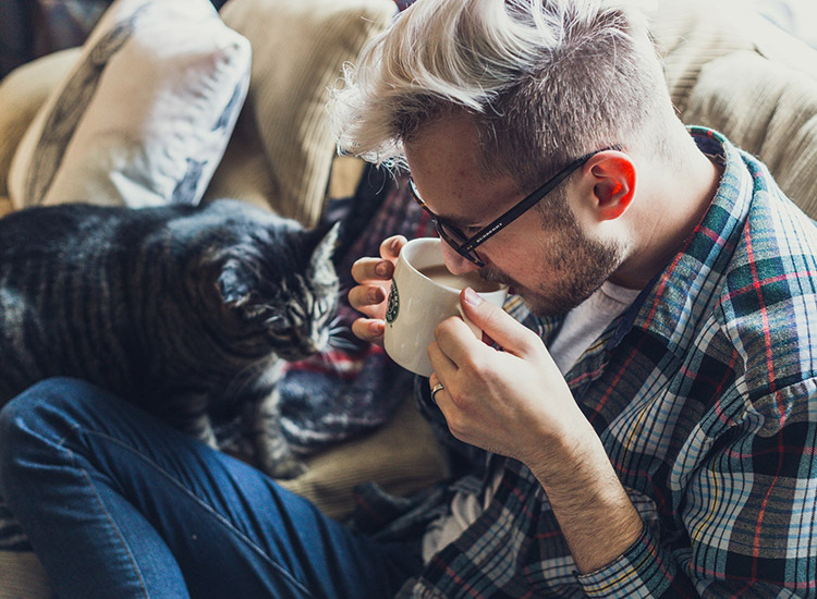 Resident enjoying his coffee with cat on his lap in his living room at 1010 Pacific Apartments