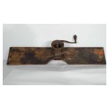 Primitive meat grinder mounted to a wooden plank.
