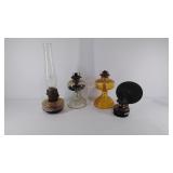 Four glass oil lamp bases, one has a shade that