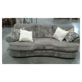 Grey sofa with four accent pillows, curved front.