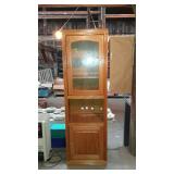 Oak cabinet with upper shelves behind glass door.