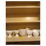 Shelf full of milk glass, mostly candle holders