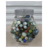 Glass jar full of assorted marbles and shooters