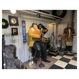 Large Elvis Presley figure with guitar, surrounded by vintage advertising signs and display pieces.