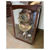 Antique deep-sea diver’s helmet displayed in a glass cabinet with maritime décor accents.