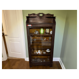 Master…Vintage curio cabinet with a dark wood finish, an arched top with decorative carvings, and a single glass door. items’s shown in pictures are sold in separate lots, see pictures for details