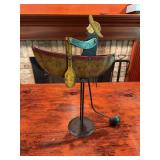 Folk art metal décor piece depicting a man in a boat. The boat is designed to balance on the metal base, giving the piece a movable or balancing display effect. Rustic decorative item suitable for fo
