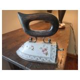 Antique sad iron with hand-painted porcelain handle and decorative metal body. May have held coal. Collectible household laundry item with ornate styling and display appeal.