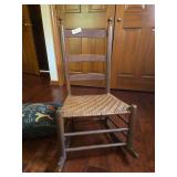 Antique children’s wooden rocking chair with spindle back and turned supports. Child-sized rocker with traditional styling and aged wear consistent with use.