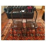 Pair of wooden dining chairs made in Malaysia with spindle backs and carved details. Features dark stained wood construction with traditional styling. Shows wear consistent with age and household use.