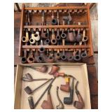 Large collection of smoking pipes with display rack. Many pipes appear older, with several having handmade or antique-style construction. Assorted group includes various pipe shapes, materials, and de