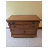 Oak dresser with two drawers over lower double-door storage. Features paneled sides, round drawer pulls, and casters. Top shows visible surface wear and finish discoloration. Measures approximately 29