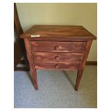 Wood nightstand with three drawers and traditional styling. Compact bedside table suitable for bedroom or accent use. Measures approximately 27 in. tall x 17 in. wide x 13 in. deep.