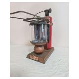 Adams Pittsburgh Sport lantern/grill with copper-tone base and burner housing, red fuel cylinder, clear cylindrical globe and overhead metal support/grill assembly. Shows finish wear, oxidation and ag