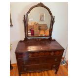 Antique four-drawer dresser with attached shaped mirror, dark wood finish, decorative drawer fronts, metal drop pulls and turned front legs. Shows age-related finish wear and surface marks.