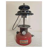 Kamplite Model RL-32B pressure lantern with red fount, black porcelain ventilator, clear heat-resistant globe and wire bail handle. Shows paint and decal wear, oxidation and general age-related use.