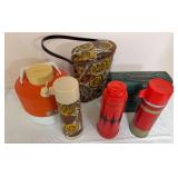 Group of vintage insulated beverage and lunch items including Thermos and Aladdin pieces, patterned carrying case, orange-and-white cooler jug and green metal lunch box. Assorted colors and styles as 