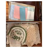 Box of assorted vintage linens including crocheted and lace doilies, embroidered pieces, cloth napkins and other textiles as shown.