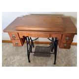 White treadle sewing machine housed in a wood cabinet with decorative carved drawer fronts, metal ring pulls and cast-iron treadle base.