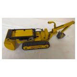 Vintage Tonka pressed-steel Trencher in yellow with rubber crawler tracks, front blade and rear digging boom with bucket. Shows general age-related paint wear and use.