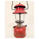 Coleman Model 200A pressure lantern marked 12/55, with red painted fount, matching red porcelain ventilator, clear Pyrex Coleman globe and wire bail handle. Shows paint wear and age-related use.