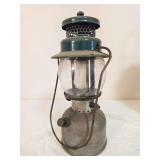 Coleman Model 242C pressure lantern marked 11/48, with silver-tone fount, green porcelain ventilator, clear Coleman globe and wire bail handle. Shows oxidation and age-related wear.