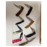 Eight assorted folding pocket and utility knives including a Buck NRA knife, NRA-ILA promotional knife and assorted modern locking and partially serrated examples. Wood, composite and metal handle sty