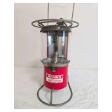 Adams 3-in-1 Sports Lantern with red body, clear cylindrical globe, metal wire stand and upper circular support; label states “Cooks – Heats – Lights.” Shows surface wear, oxidation and age-re
