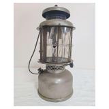 Coleman Model QL pressure lantern with silver-tone fount, mica globe assembly and metal bail handle. Mica panels show age-related deterioration and damage, with oxidation and surface wear throughout.