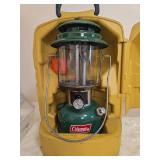 Coleman Model 220J Lantern with Yellow Carrying Case – Marked 4/76. Green double-mantle pressure lantern with clear globe and wire bail handle, housed in a yellow molded Coleman carrying case.