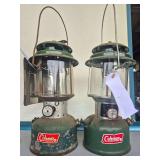 Coleman Models 220H & 220F Lanterns – Marked 2/74 & 2/66. Green double-mantle pressure lanterns with clear globes and wire bail handles; one fitted with reflector panels, with age-related paint wear