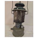 Coleman Model 220D pressure lantern with silver-tone fount, green porcelain ventilator, segmented mica globe and wire bail handle. Shows oxidation and general age-related wear.