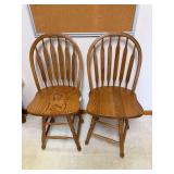Pair of tall oak bar stools with spindle backs, shaped solid wood seats, turned legs and stretcher bases.