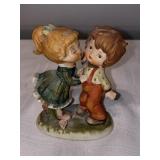 K- little girl trying to kiss little boy figurine