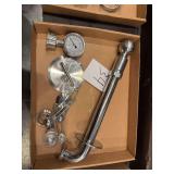 industrial or laboratory metal components, including a pipe section, a pressure gauge, a lid, and measuring tools.