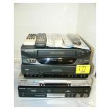 STACK OF VCRs, DVD PLAYETRS, AND REMOTES