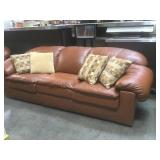 Overstuffed brown leather sofa w/ throw pillows.