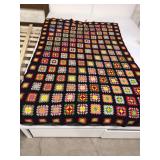 This is a handmade vintage granny square crochet afghan blanket featuring colorful patchwork squares on a black background.