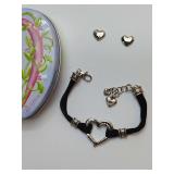 Brighton Heritage Heart Bracelet featuring a sculptural silver-plated heart centerpiece on black corded strands, with Brighton Retired "Penelope" heart pierced earrings, and a Gift Can.