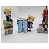 Porcelain hinged trinket boxes, Madeline on a flower cart with her dog, Madeline in front of a book titled "MADELINE" with an Eiffel Tower illustration, and Miniature Lighthouse. The lighthouse is emp