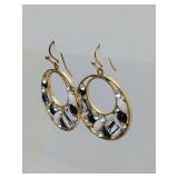 Gold-toned dangle hoop earrings feature a decorative filigree design inlaid with black, white, and clear crystals. 1 3/4" long.