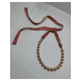 Vintage-style beaded necklace featuring champagne or rose gold-colored faux pearls on a ribbon or cord tie closure. Has stain on one tie, see pic