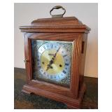 Vintage Benchmark oak wooden bracket mantel clock, brass carrying handle and an ornate gold-tone etched dial face. 15"T x 11"W x 6"D. Franz Hermle 2 Jewels, Made in West Germany. No key.